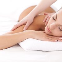 25052571 - total relaxation. beautiful young woman lying on front and looking at camera while massage therapist massaging her shoulders