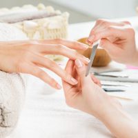 Closeup shot of a woman in a nail salon receiving a manicure by a beautician with nail file. Woman getting nail manicure. Beautician file nails to a customer. Shallow depth of field with focus on nailfile.