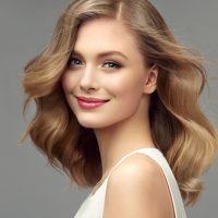 Model with dark blonde hair. Frizzy, elegant hairstyle is surrounding lovely face of tenderly smiling young woman. Natural gloss and softness of healthy hair. Hair care and hairdressing art.
